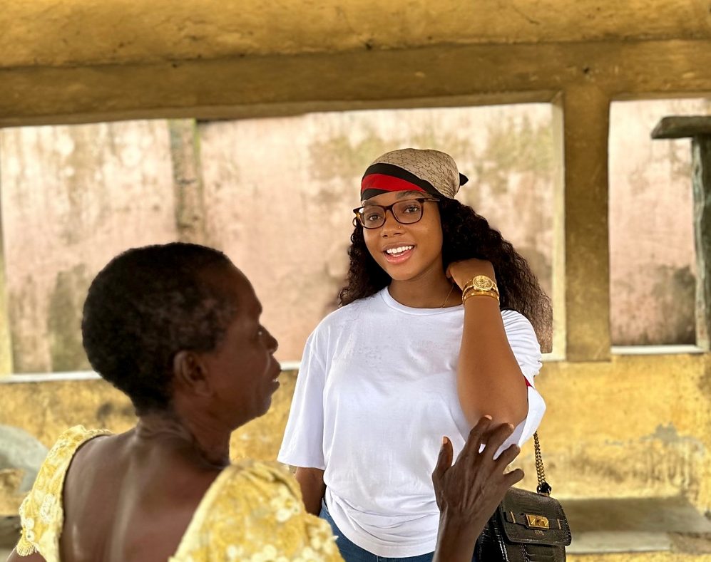 A smiling woman in a white shirt speaks with an older woman in a yellow blouse.