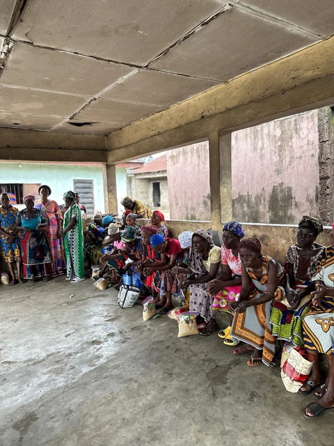 Older women sit in a row with bags of food while other women stand nearby.