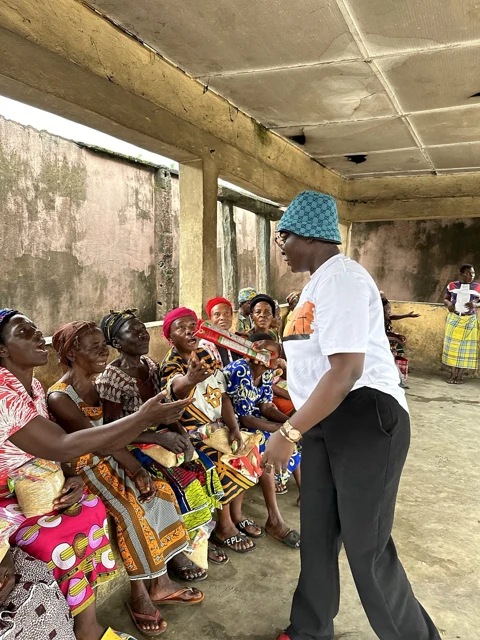 A woman in a blue hat hands packaged food to women seated with bags of supplies.