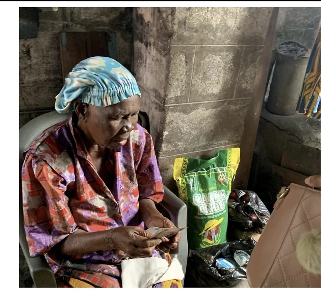 An older woman sits holding banknotes beside a bag of rice and other bags.